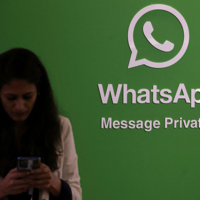 A woman uses her phone next to a logo of the WhatsApp application during Global Fintech Fest in Mumbai