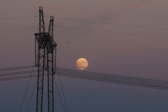 Full moon rises behind an electricity pylon with high-voltage power lines in Dnipropetrovsk region