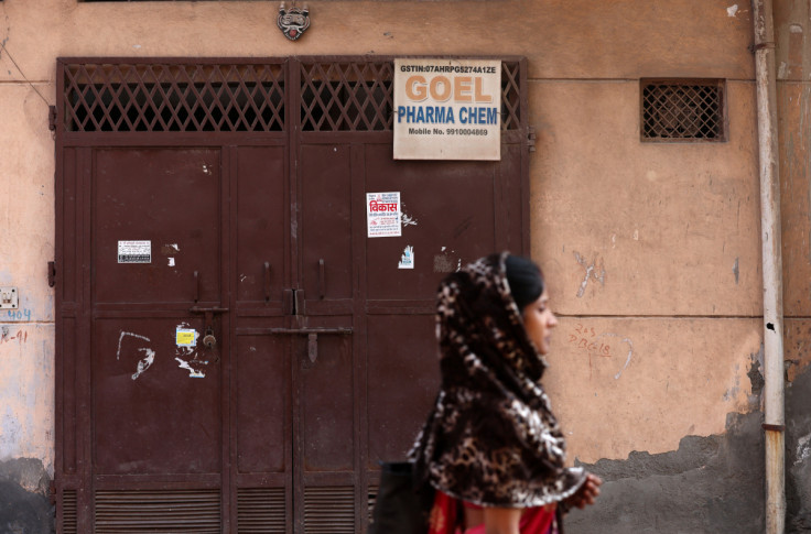 A woman walks past the closed gate of Goel Pharma Chem, in New Delhi