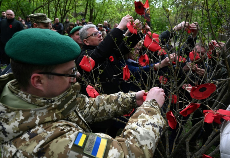 People decorate a 'memory tree' with paper red poppies at the location of the former Stalag 328 prisoner of war camp in Lviv, western Ukraine