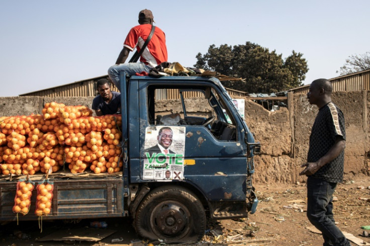 An orange seller sits atop a truck with a ruling party campaign poster on it at Harare's Musika market