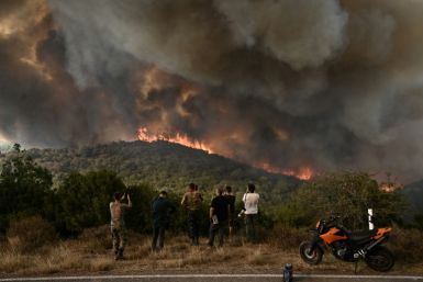 People look at a wildfire raging in a forest in northern Greece
