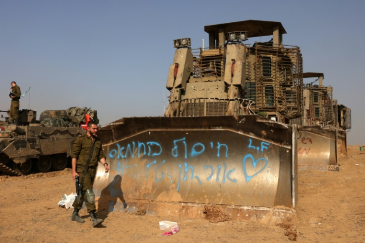 Israeli troops and military vehicles are positioned near the border with the Gaza Strip. The graffiti in blue reads in part "eliminate Hamas"
