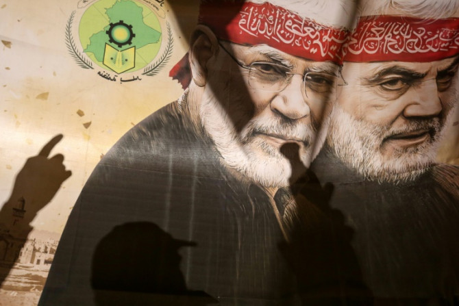 Supporters of pro-Iran factions gesture in front of a poster bearing an image of slain top Iranian commander Qasem Soleimani and Iraqi commander Abu Mahdi al-Muhandis in Baghdad's Tahrir Square on January 13, 2024