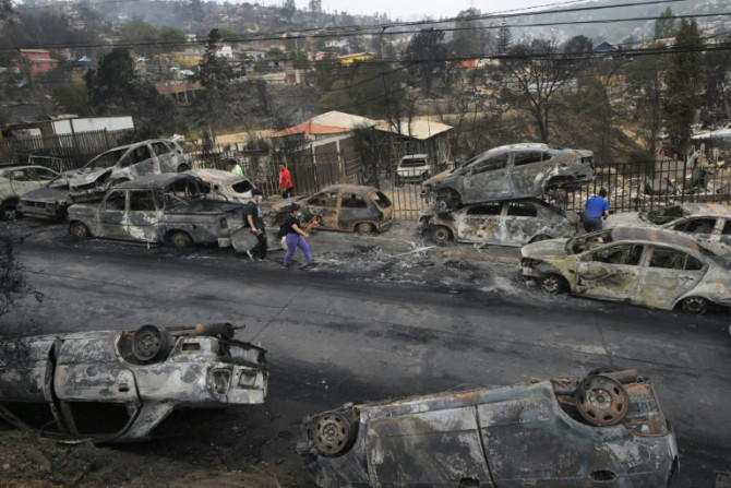 Survivors walk past burned out vehicles after a wildfire ravaged Quilpue, in Chile's Vina del Mar region