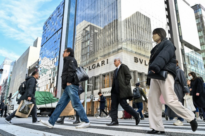Pedestrians cross the street in front of luxury shops in the Ginza shopping district in Tokyo on January 19, 2024