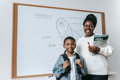 Cheerful Black woman with student against whiteboard. Representational Image.