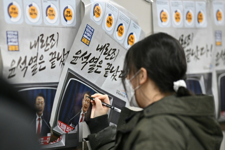 A woman writes on a poster showing South Korea President Yoon Suk Yeol, with text that reads 'insurrection criminal Yoon is over'