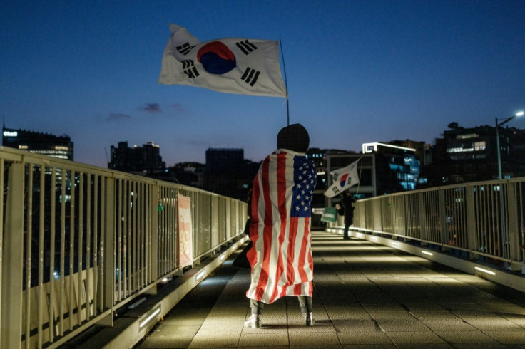A supporter of impeached South Korean President Yoon Suk Yeol draped in a US flag waves South Korea's in the capital Seoul